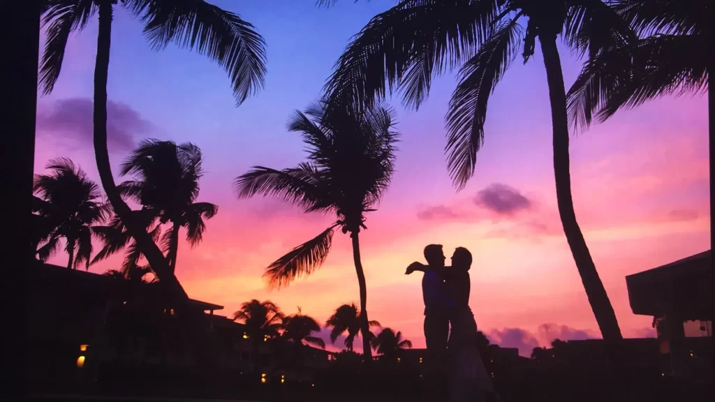 A silhouette of a family photographer in Cancun holding a child aloft against a dramatic purple and pink sunset sky, framed by swaying palm trees.
