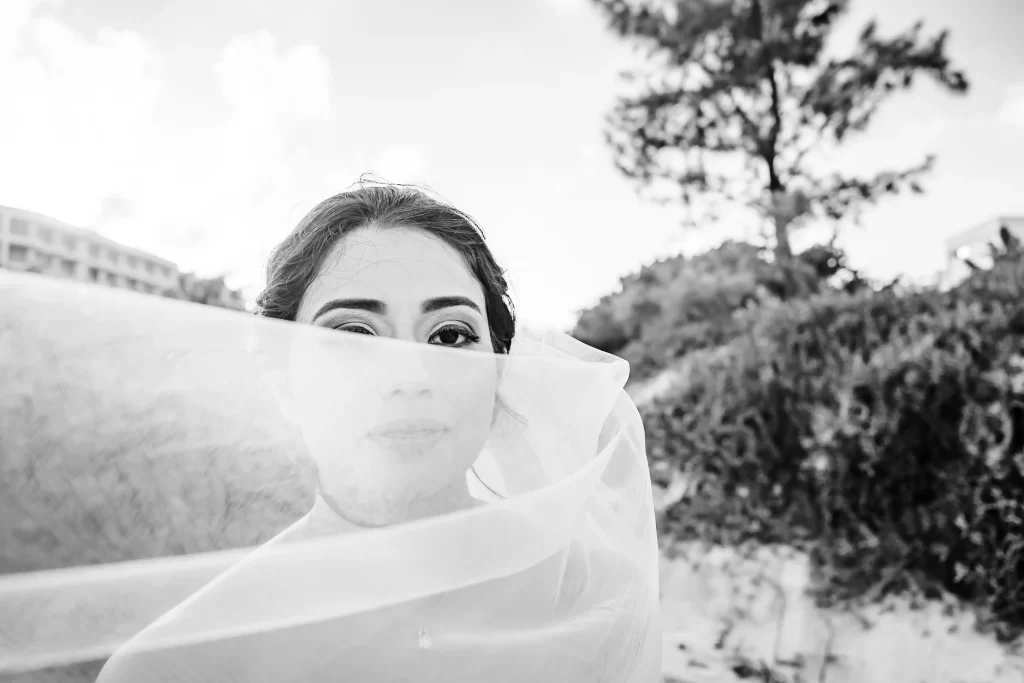 A monochrome portrait of a woman with her gaze piercing through a delicate veil, capturing a moment of serene elegance amidst the tranquil outdoor setting of Cancun.