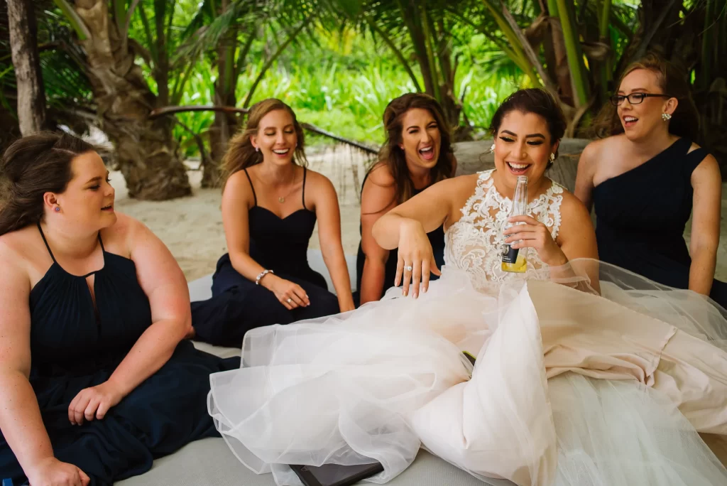 A joyful bride in a white gown shares a laugh with her bridesmaids dressed in elegant black dresses, as they enjoy a light-hearted moment together amidst lush greenery, captured perfectly by a Wedding photographer in